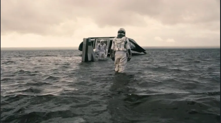 Astronauts wading through the shallow ocean on Miller’s planet